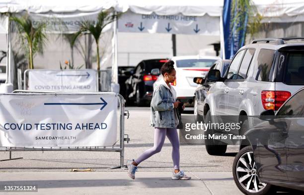 Pedestrian walks past cars lined up at a drive-through COVID-19 testing center on December 06, 2021 in Los Angeles, California. New requirements...