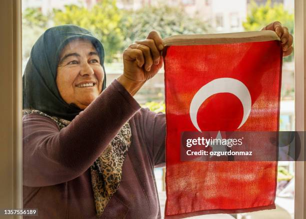 mujer turca de alto rango lleva un pañuelo en la cabeza que cuelga una bandera turca en la ventana - bandera turca fotografías e imágenes de stock