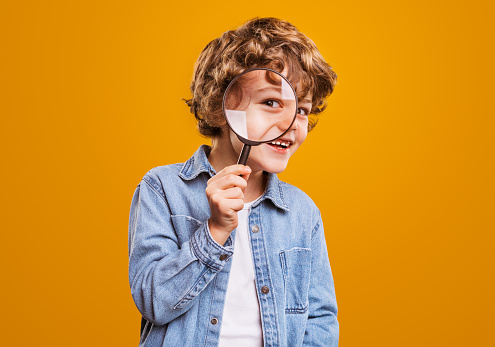 Cheerful boy with magnifying glass looking at camera