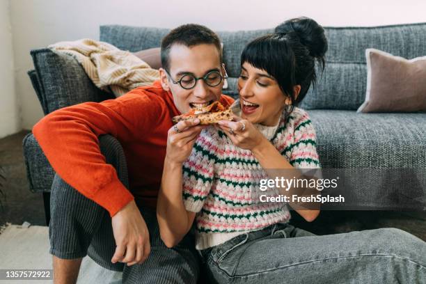 a caring wife sharing a piece of pizza with her husband - sharing pizza stock pictures, royalty-free photos & images