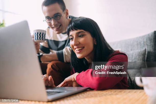 una donna curiosa che scorre qualcosa sul suo laptop mentre suo marito sta guardando - couple looking laptop foto e immagini stock