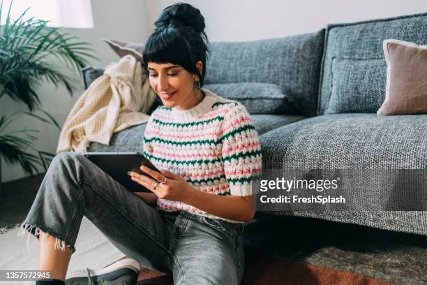 eine junge frau sitzt auf dem boden und schaut sich einen podcast auf ihrem tablet an - reading stock-fotos und bilder