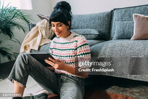 Una joven sentada en el suelo y viendo un podcast en su tableta Una joven sentada en el suelo y viendo un podcast en su tableta