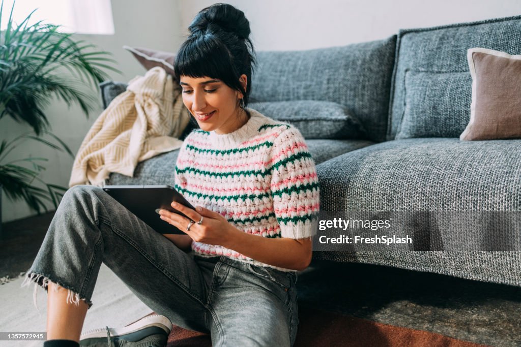 A Young Female Sitting On The Floor And Watching A Podcast On Her Tablet