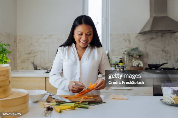 smiling woman preparing healthy meal in her kitchen - beautiful filipina woman stock pictures, royalty-free photos & images