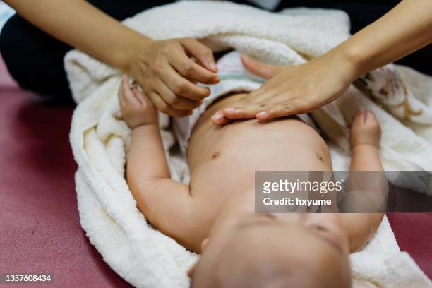 mother massaging her baby boy on bed - baby abdomen stock pictures, royalty-free photos & images