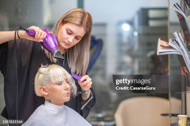 jeune coiffeuse séchant les cheveux d’un client - coiffeur photos et images de collection