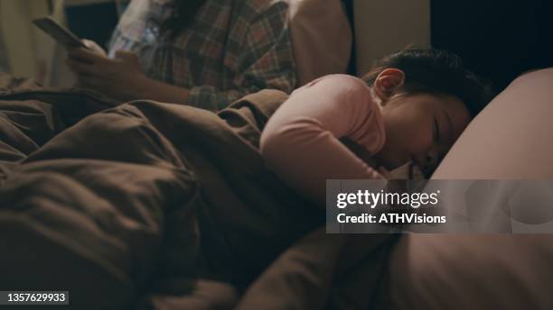 mother using smart phone while daughter sleeping at night. - maxim stock pictures, royalty-free photos & images