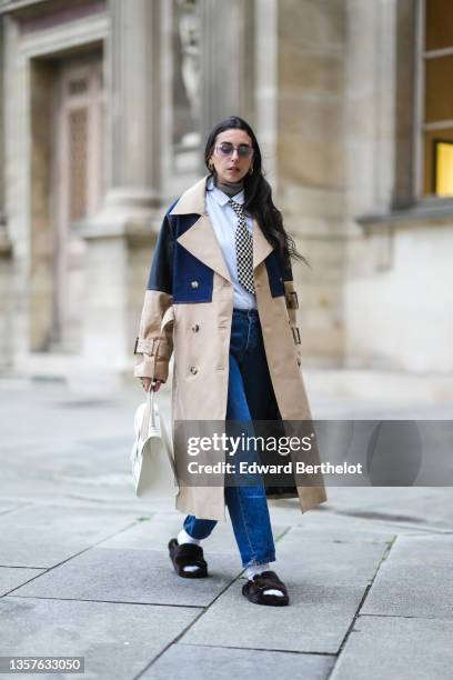 Gabriella Berdugo wears sunglasses from Gucci, gold earrings, a brown ribbed wool turtleneck pullover, a white shirt from Wrangler, a black and white...