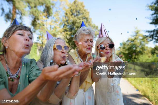 senior women friends having birthday party outdoors blowing confetti. - tierfreundschaften stock-fotos und bilder