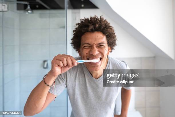 male with funky hair tooth brushing routine in a bathroom front teeth brushing looking in mirror - brush teeth stock pictures, royalty-free photos & images