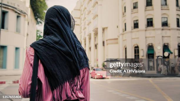 happy and smiling muslim tourist listening music and looking on mobile phone while walking on the street. good life - véu imagens e fotografias de stock