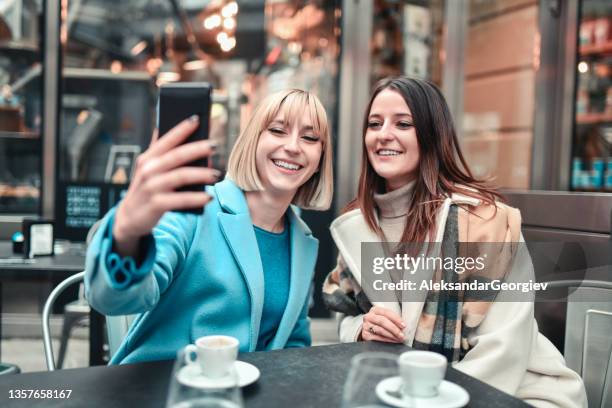 smiling female friends taking cute coffee time selfie in outdoor bar - crowded cafe stock pictures, royalty-free photos & images