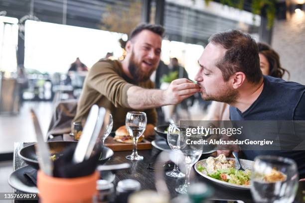 hombre gay alimentando a su novio mientras disfruta de un almuerzo de ensalada con amigas - male burger eating fotografías e imágenes de stock