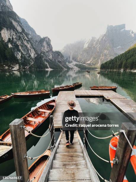 rear view of adult man with sunshade walking along the jetty of lago di braies at sunrise - wood pier stock pictures, royalty-free photos & images