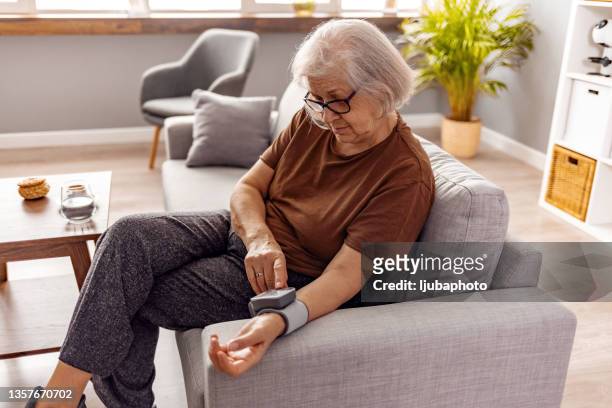ältere frau, die ihren blutdruck zu hause überprüft - blood pressure stock-fotos und bilder