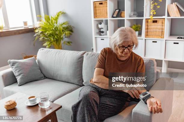 femme âgée assise tout en mesurant sa tension artérielle dans le salon - blood pressure photos et images de collection