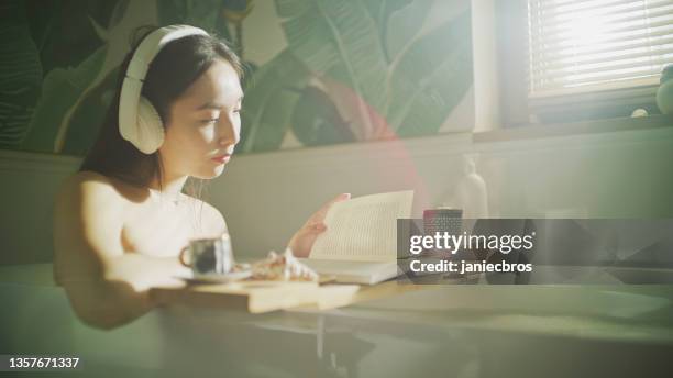 reading in the bathtub. asian woman relaxing with coffee and snacks - bad thoughts stockfoto's en -beelden