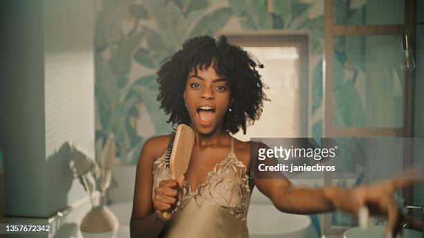feeling fabulous. african ethnicity woman enjoying morning bathroom routine and having fun in front of mirror. singing to a hairbrush and dancing vigorously - woman in bathroom stock pictures, royalty-free photos & images