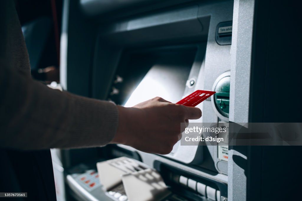 Close up of young woman inserting her bank card into automatic cash machine in the city. Withdrawing money, paying bills, checking account balances, transferring money. Privacy protection, internet and mobile security concept