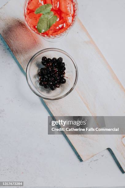 top down image of aronia berries in a bowl beside a cold, refreshing berry drink - aronia berry stock-fotos und bilder