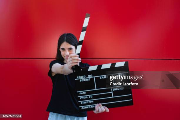 a young girl holding a movie clapboard in front of a red background. - young film director stock pictures, royalty-free photos & images