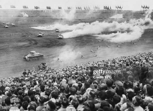 Spectators look on from the grandstand as a formation of Wehrmacht Panzerkampfwagen I Ausf A light tanks and Infantry soldiers perform a military...