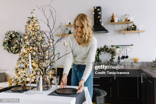 young woman putting the finishing touches to a decorated christmas table - hanging christmas lights stock-fotos und bilder