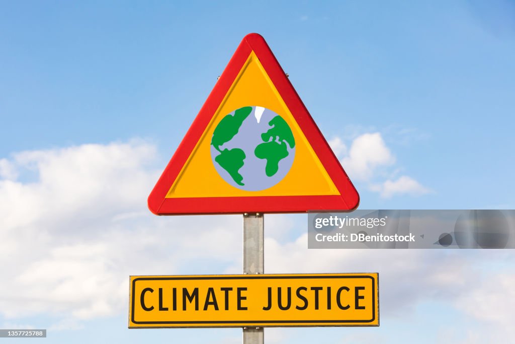 Red and yellow danger road sign with the planet Earth and a sign that reads "Climate Justice" with the sky in the background. Ecology, climate change and global warming concept