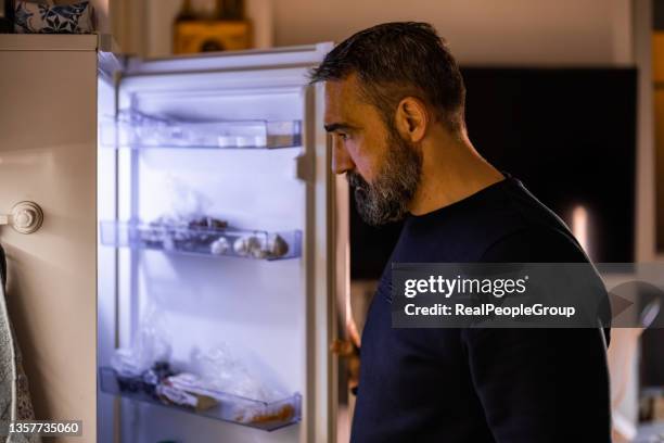 portrait of a mature man taking food from refrigerator - single adults eating dinner at home stock pictures, royalty-free photos & images