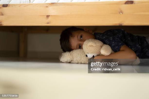 child hiding under the bed - boy sitting on floor stockfoto's en -beelden