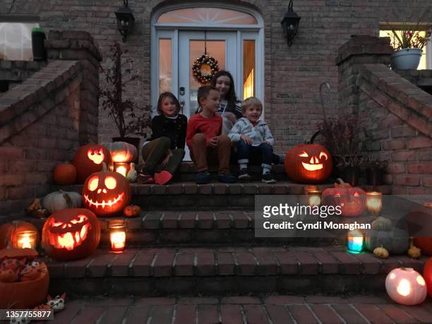cousins sitting together on a staircase with halloween jack o'lanterns glowing - schnitzen stock-fotos und bilder