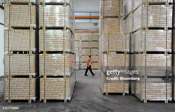 An employee passes palettes of wood laminate flooring packaged for shipping in a warehouse at the Tarkett Group factory in Backa Palanka, Serbia, on...