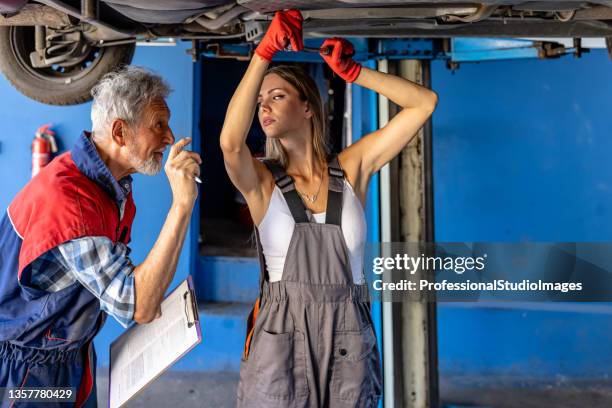 a couple of auto mechanics is fixing exhaust system under the lifted car with the control of their older manager. - old garage at home stock pictures, royalty-free photos & images