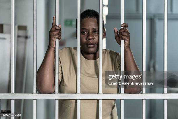 junge afro-frau, die ernsthaft und verzweifelt hinter gittern aussieht, die gefängnisgitter oder die eines sicherheitstors sein können - woman prison stock-fotos und bilder