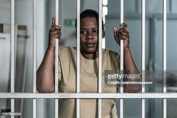刑務所のバーやセキュリティゲートのものかもしれないバーの後ろに深刻で絶望的に見える若いアフロの女性 - 鉄格子 ストックフォトと画像