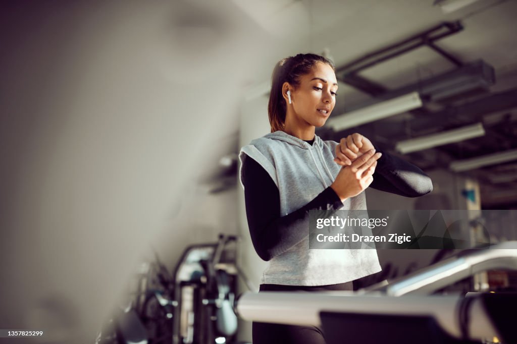 Young sportswoman using fitness tracker while exercising on treadmill in a gym.