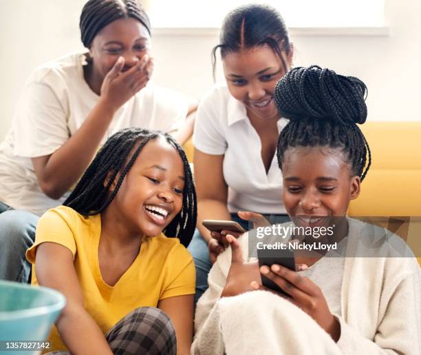 group of teenage girls looking at photos on phone and smiling at home - braided hairstyles for african american girls stock pictures, royalty-free photos & images