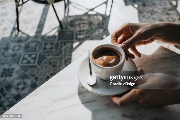 close up of woman's hand holding a cup of coffee, drinking coffee in outdoor cafe against beautiful sunlight, having a relaxing moment. enjoying life's simple pleasures - koffie stockfoto's en -beelden