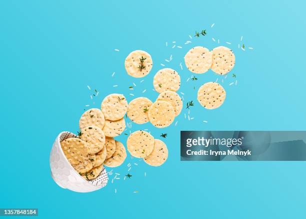 flying bowl with rice crackers,  white rise and thyme branches over blue background. levitation food composition with copy space - crackers stock pictures, royalty-free photos & images