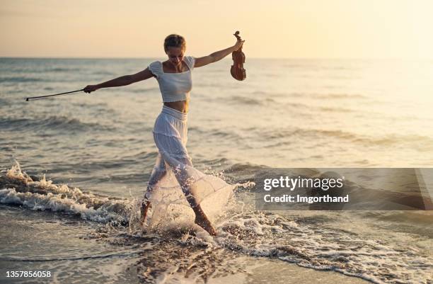 teenage girl walking with violin on the beach on sunset - young violinist stock pictures, royalty-free photos & images