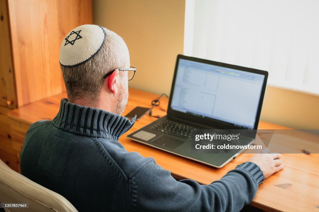 Jewish man wearing skull cap working from home