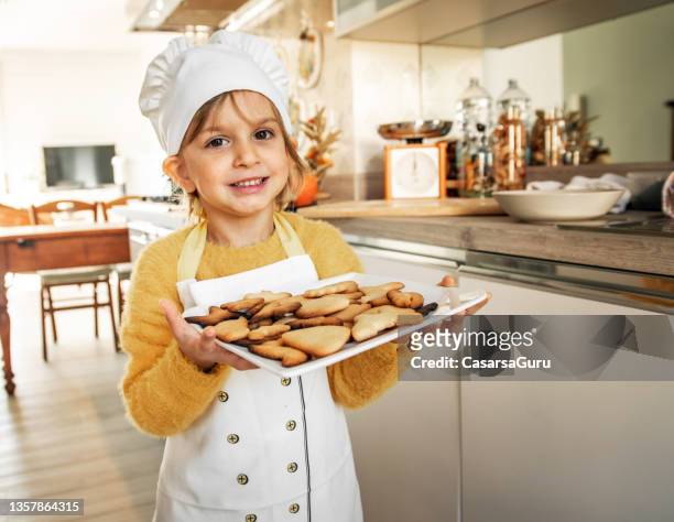 proud little girl cook portrait holding homemade cookies in a domestic kitchen - kid chef stock pictures, royalty-free photos & images