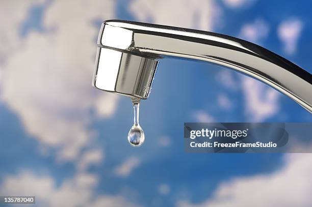 single water drop from stainless faucet; clouded blue sky background - slow motion water stock pictures, royalty-free photos & images
