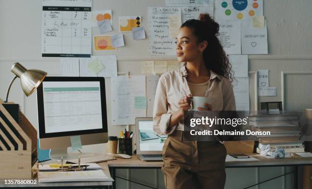 scatto di un'attraente giovane donna d'affari in piedi e con lo aspetto contemplativo mentre tiene in mano una tazza di caffè nel suo ufficio di casa - workforce foto e immagini stock