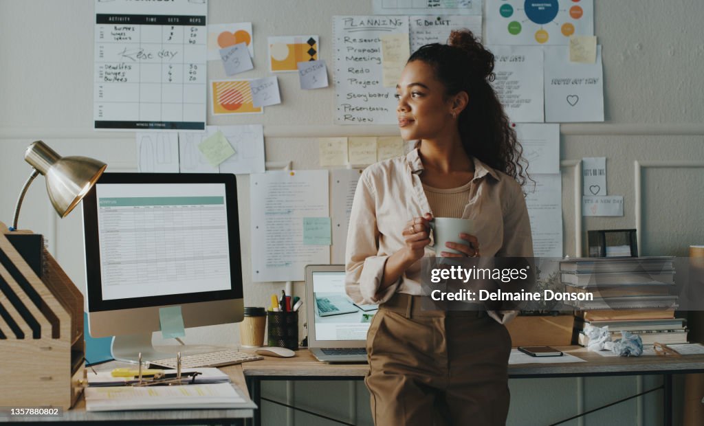 Shot of an attractive young businesswoman standing and looking contemplative while holding a cup of coffee in her home office