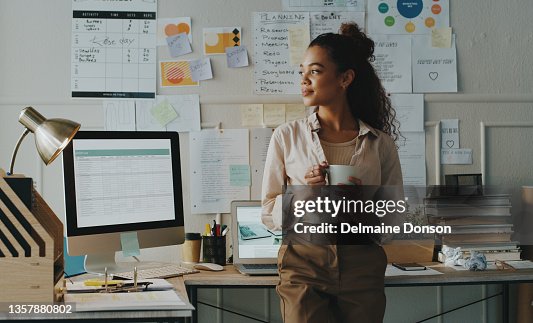 Shot of an attractive young businesswoman standing and looking contemplative while holding a cup of coffee in her home office Shot of an attractive young businesswoman standing and looking contemplative while holding a cup of coffee in her home office