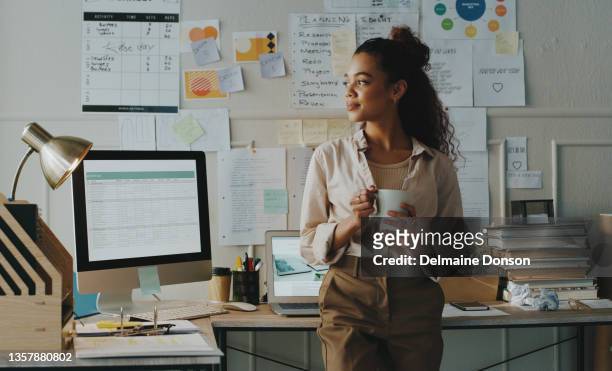 shot of an attractive young businesswoman standing and looking contemplative while holding a cup of coffee in her home office - werken stockfoto's en -beelden