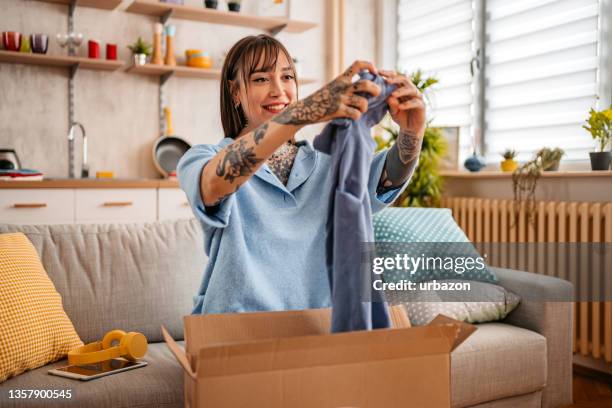 woman unpacking package with new t-shirt at home - clothing stock pictures, royalty-free photos & images