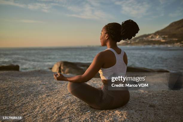 full length shot of an attractive young woman practising yoga on the beach - meditação imagens e fotografias de stock